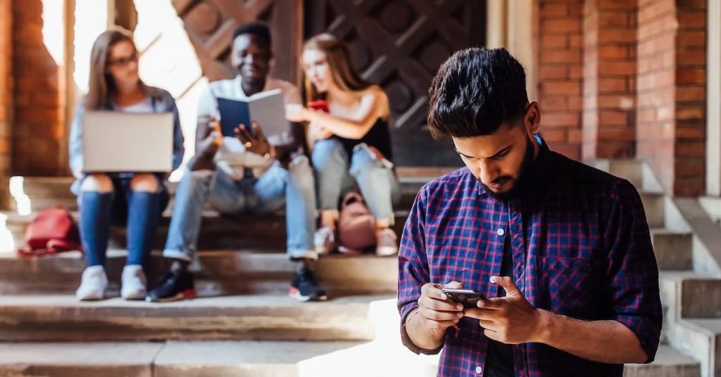 a man looking at his phone with people in background reading book