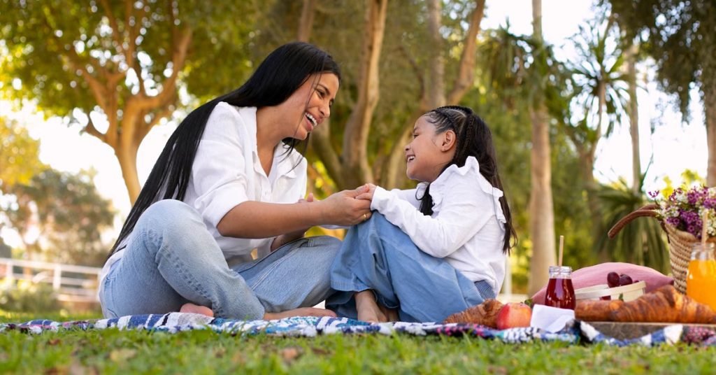 a woman and a girl sitting on a blanket in a park