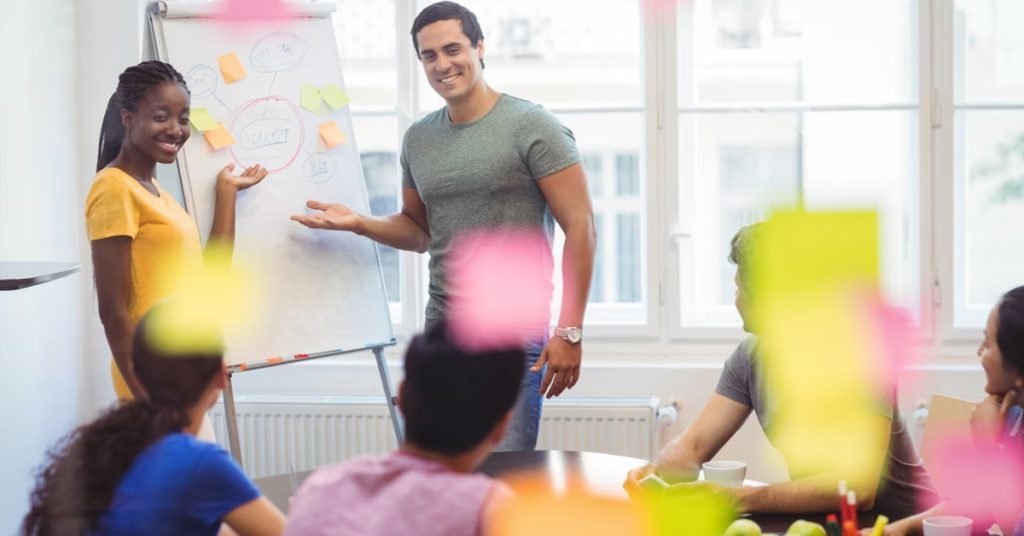 a man and a women standing in front of a whiteboard with people around it