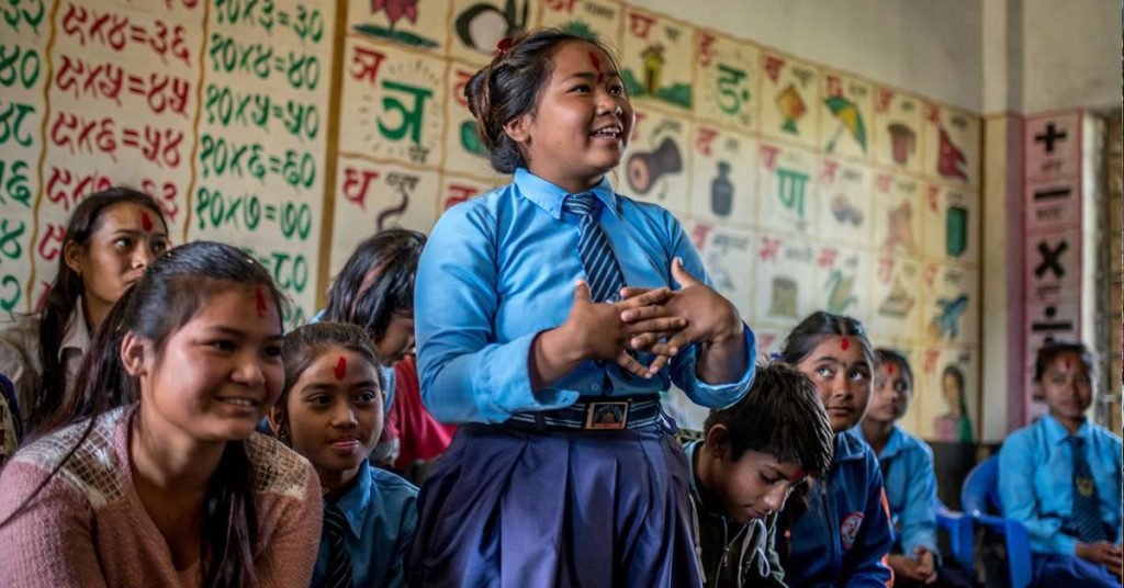 a girl in her school uniform standing in a classroom with other children